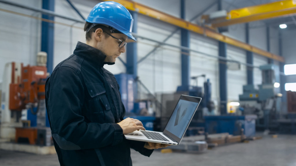 Man in shop working on laptop while wearing a hardhat